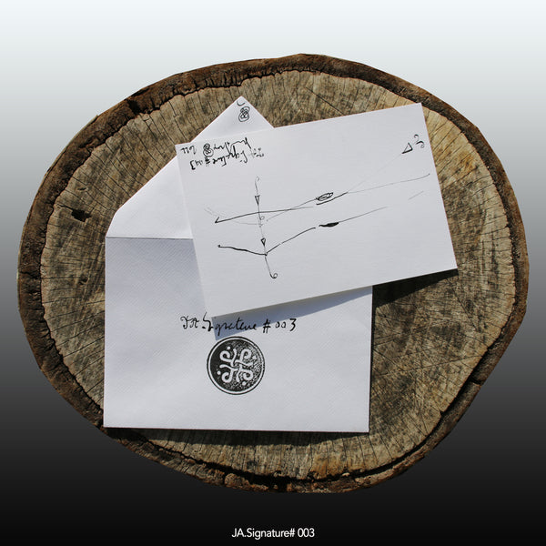 JA.SIGNATURE#003 NFT created from the physical collection JA.Signature by James Arax. On the picture : On a log, in the foreground the JA.Signature paper card and below the envelope with the number of the NFT t and james sign (LogoType).